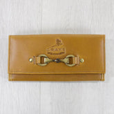 Antique tan leather purse with a metallic bit closure and embossed logo, displayed on a wooden surface.