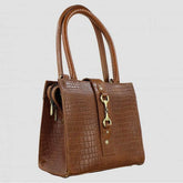 A brown natural leather handbag with a crocodile pattern, featuring a zipped top, detachable handle, and protective feet on the base.