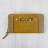 A tan leather and suede purse with a metal snaffle bit detail and zipper closure, displayed on a wooden surface.