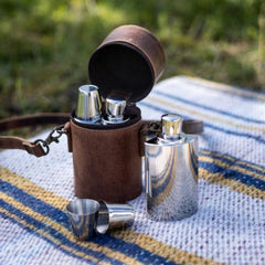 sterling silver whiskey flask and shot glasses on a cloth outdoors