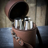 A brown leather travel whisky set open, showing three stainless steel flasks inside.