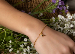 Gold bracelet on a wrist with a natural background of flowers and greenery