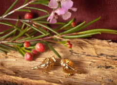 Gold bird-shaped earrings on a wooden surface with pink flowers and red berries in the background.