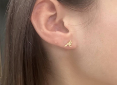 Gold earring worn on an ear with a blurred background