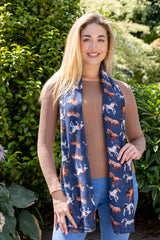 A woman wearing a navy scarf with a horse pattern, paired with a brown top and blue jeans.