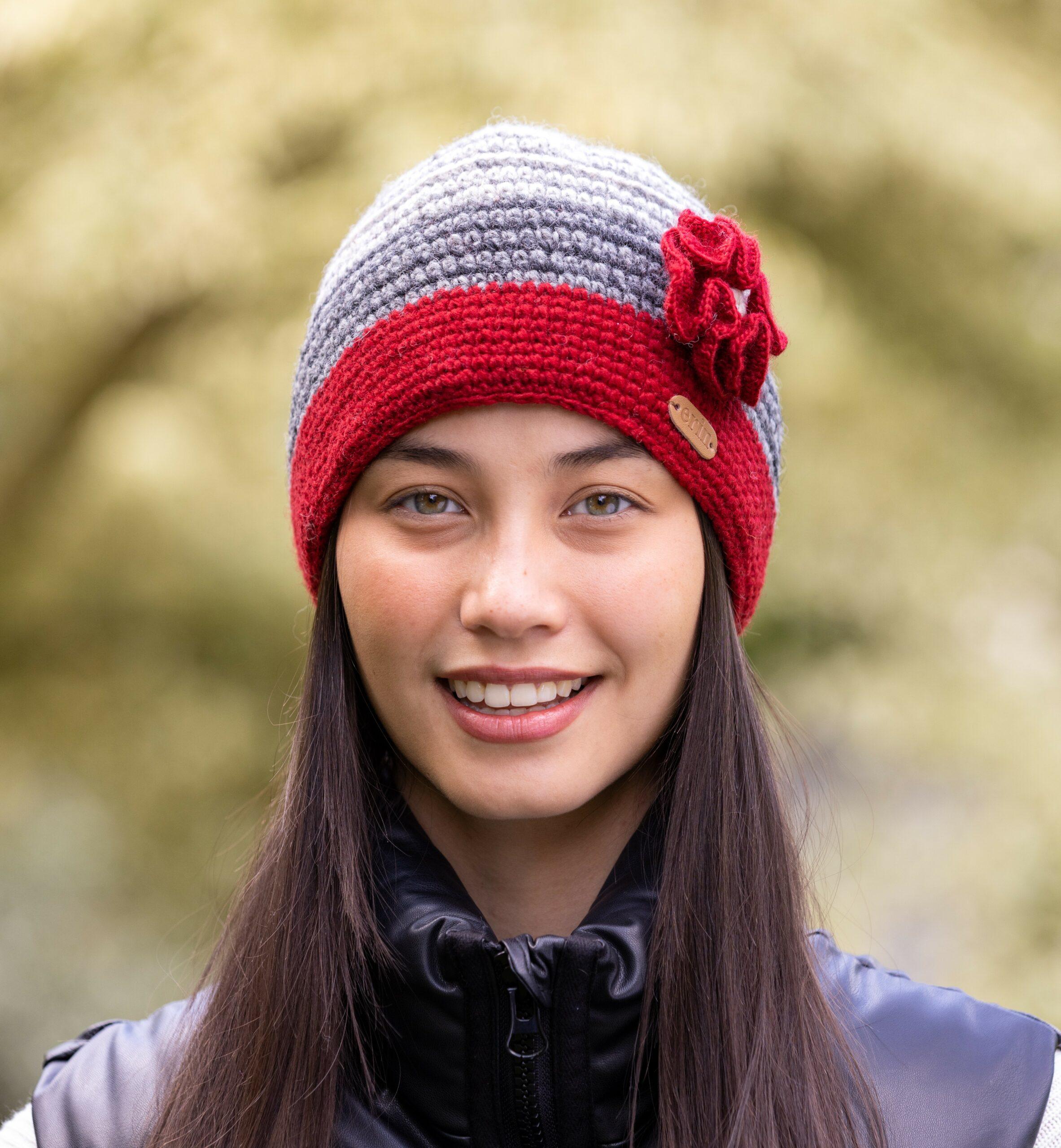 A woman wearing a red and grey crochet knitted cap with a knitted flower corsage on the side.
