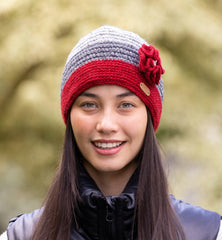 A woman wearing a red and grey crochet knitted cap with a knitted flower corsage on the side.