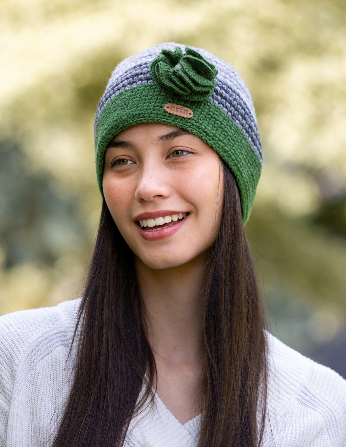A woman wearing a green and grey crochet knitted cap with a knitted flower corsage on the side.