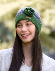 A woman wearing a green and grey crochet knitted cap with a knitted flower corsage on the side.