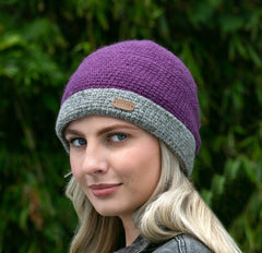 A woman wearing a purple crochet turn up hat with a gray brim.