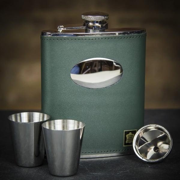 A green leather hip flask set with stainless steel cups and a pouring funnel, displayed on a dark background.