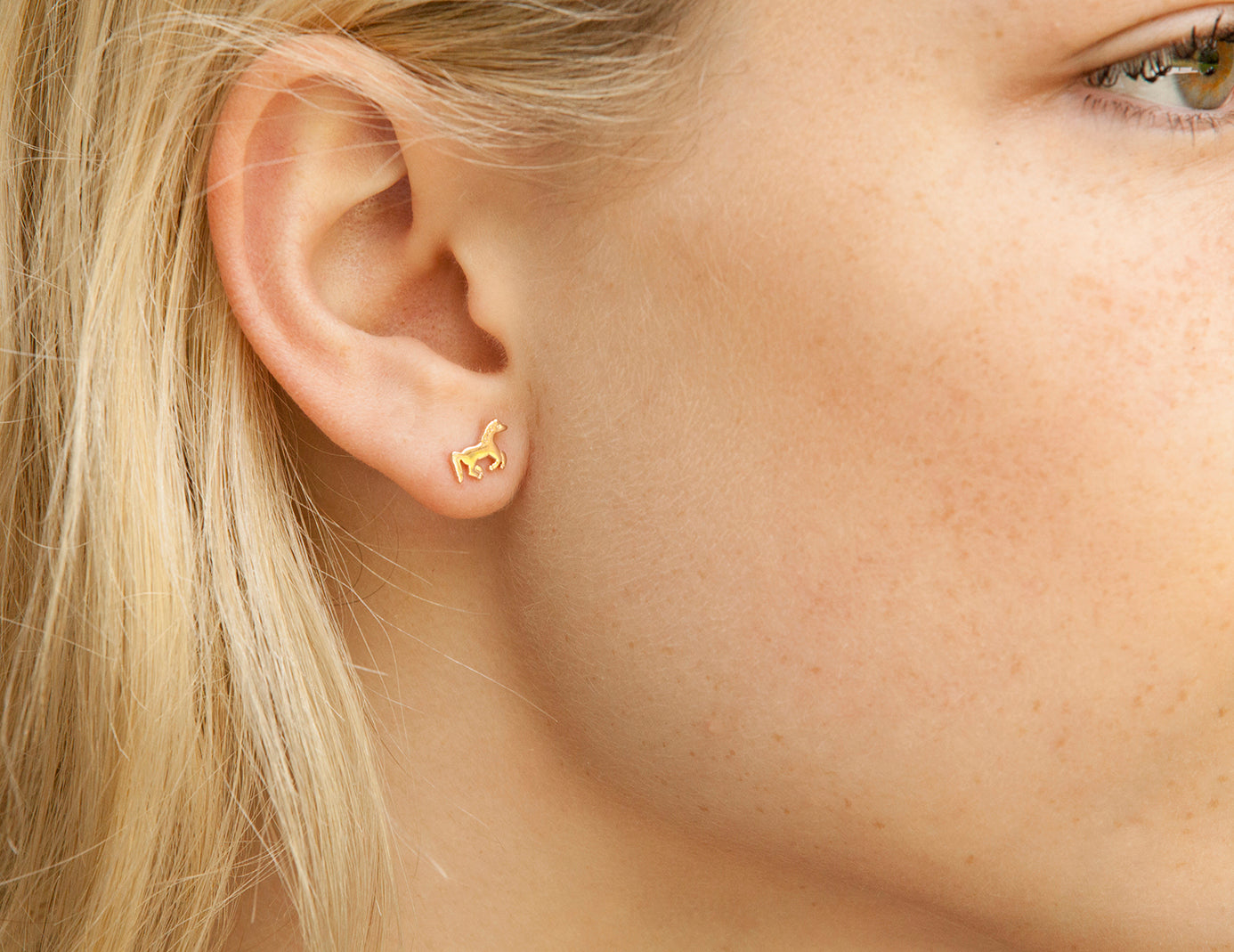 Close-up of a person wearing a gold earring with a small design.