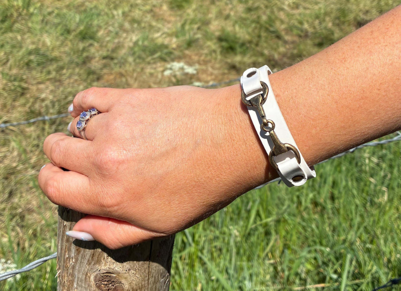 Hand wearing a silver bracelet holding onto a wooden post with grass in the background