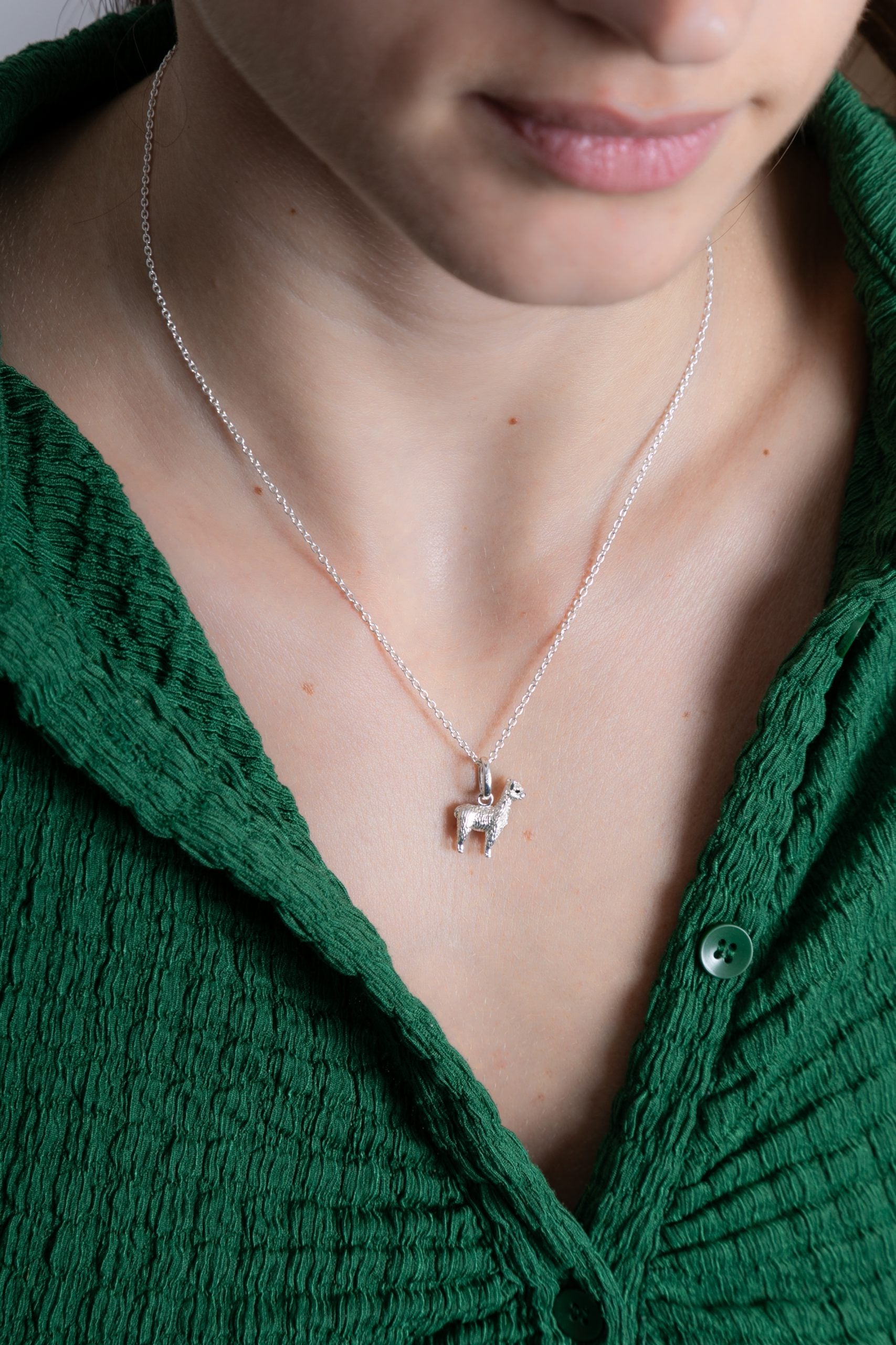 Close-up of a person wearing a green top with a necklace featuring a small pendant.