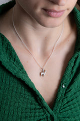 Close-up of a person wearing a green top with a necklace featuring a small pendant.