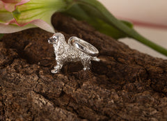 Silver dog-shaped ring on a wooden surface with a blurred flower in the background