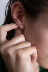 Close-up of an ear with a small gold earring, held by a hand.