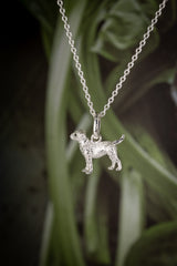 Silver dog-shaped pendant on a chain against a plant background