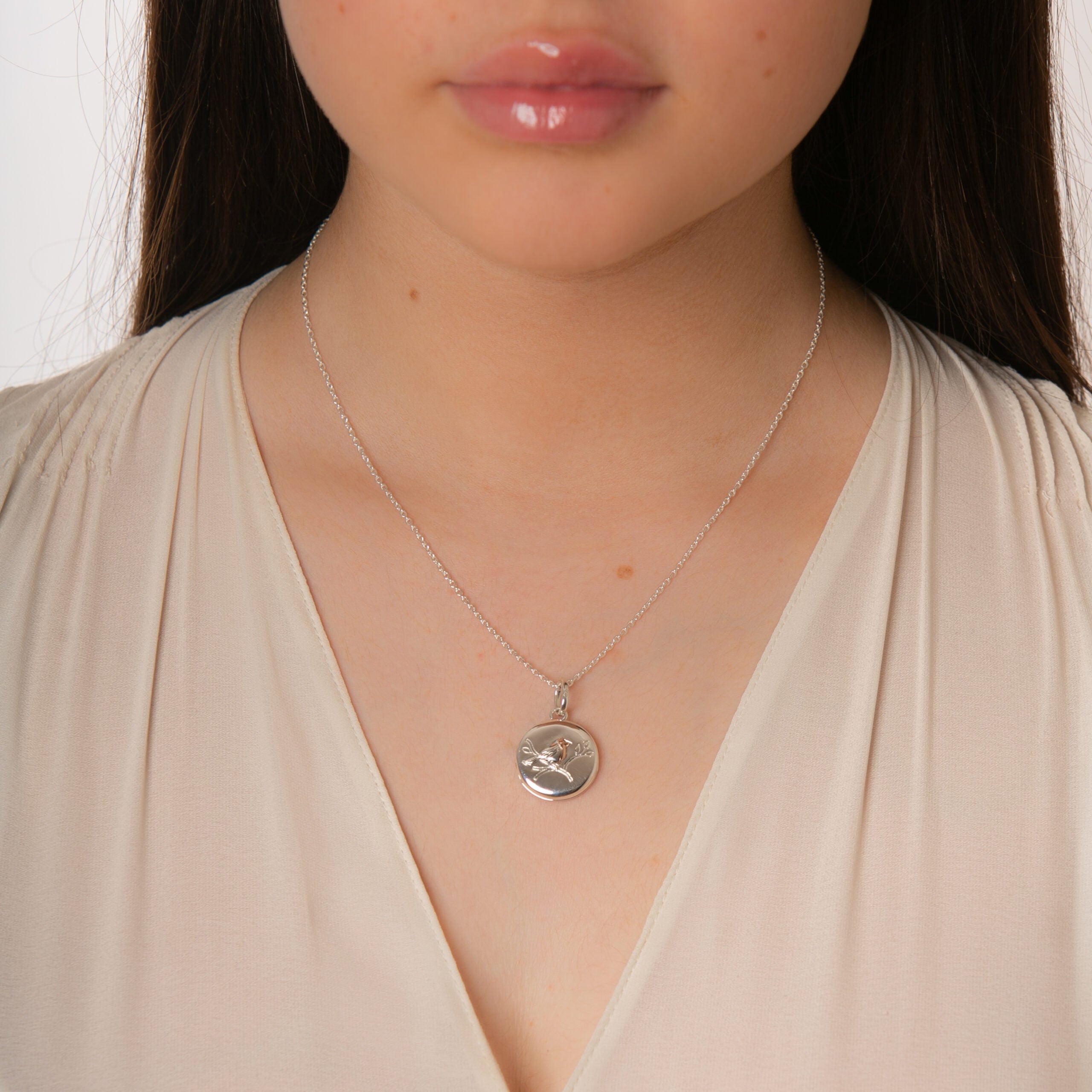 Close-up of a person wearing a silver necklace with a pendant against a neutral background