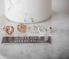 Four pairs of horseshoe-shaped earrings on a 'GALLOP COLLECTION' stand with a marble background.