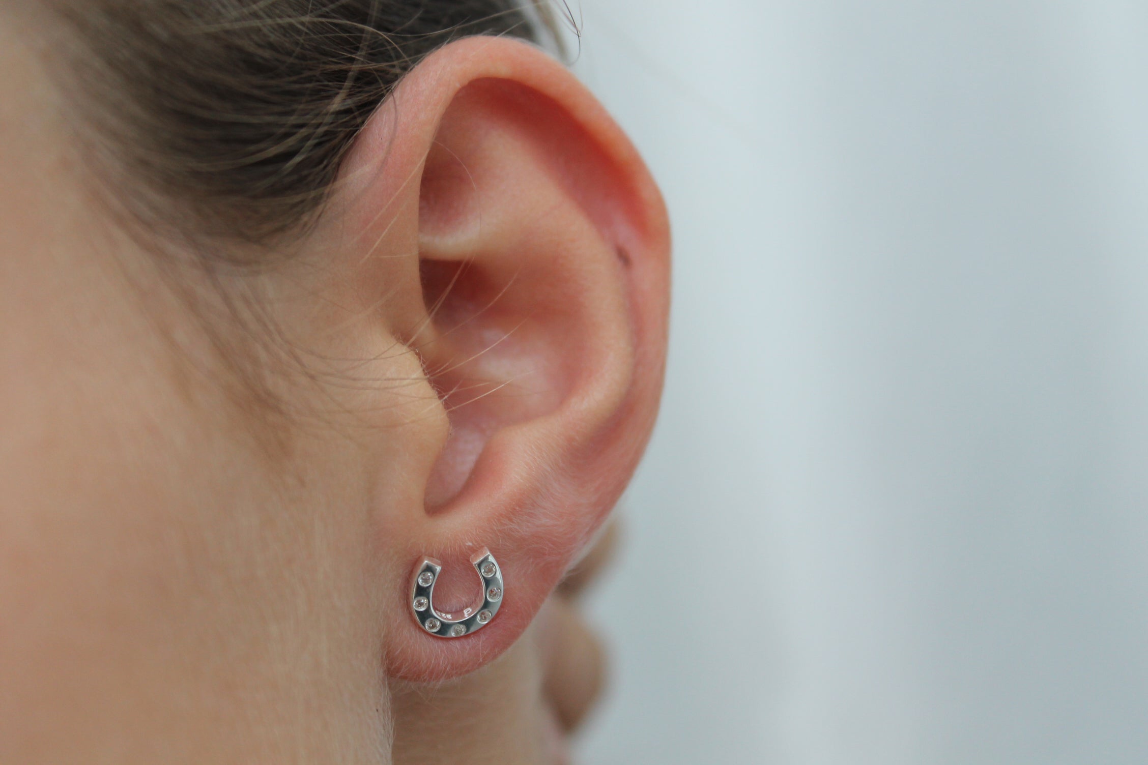 Close-up of an ear wearing a silver horseshoe earring on a plain background