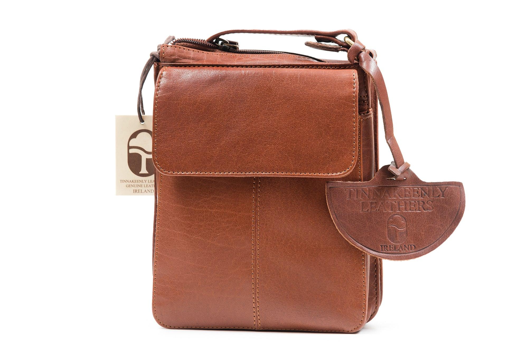 A soft tan brown leather shoulder bag with a zipper closure, front pocket with a flap, and an adjustable crossbody strap, displayed against a white background.